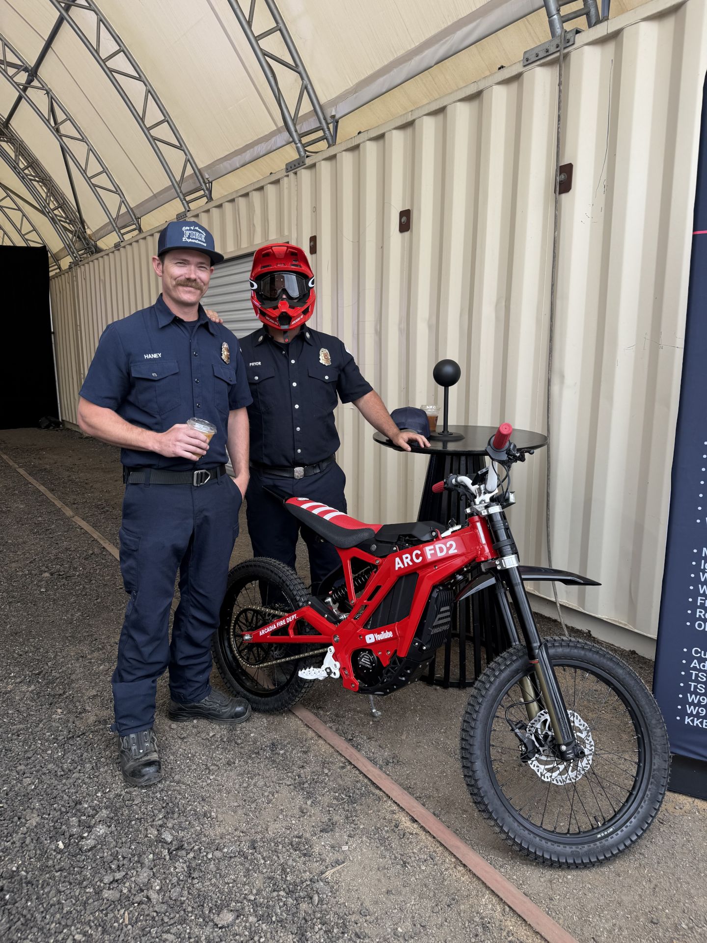 Two firefighters, one standing one on a bike.